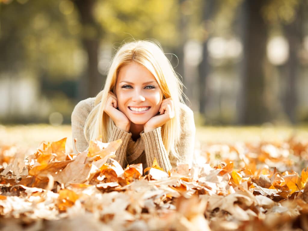 Beautiful,Blond,Hair,Woman,Sitting,On,Leaves,At,The,Park